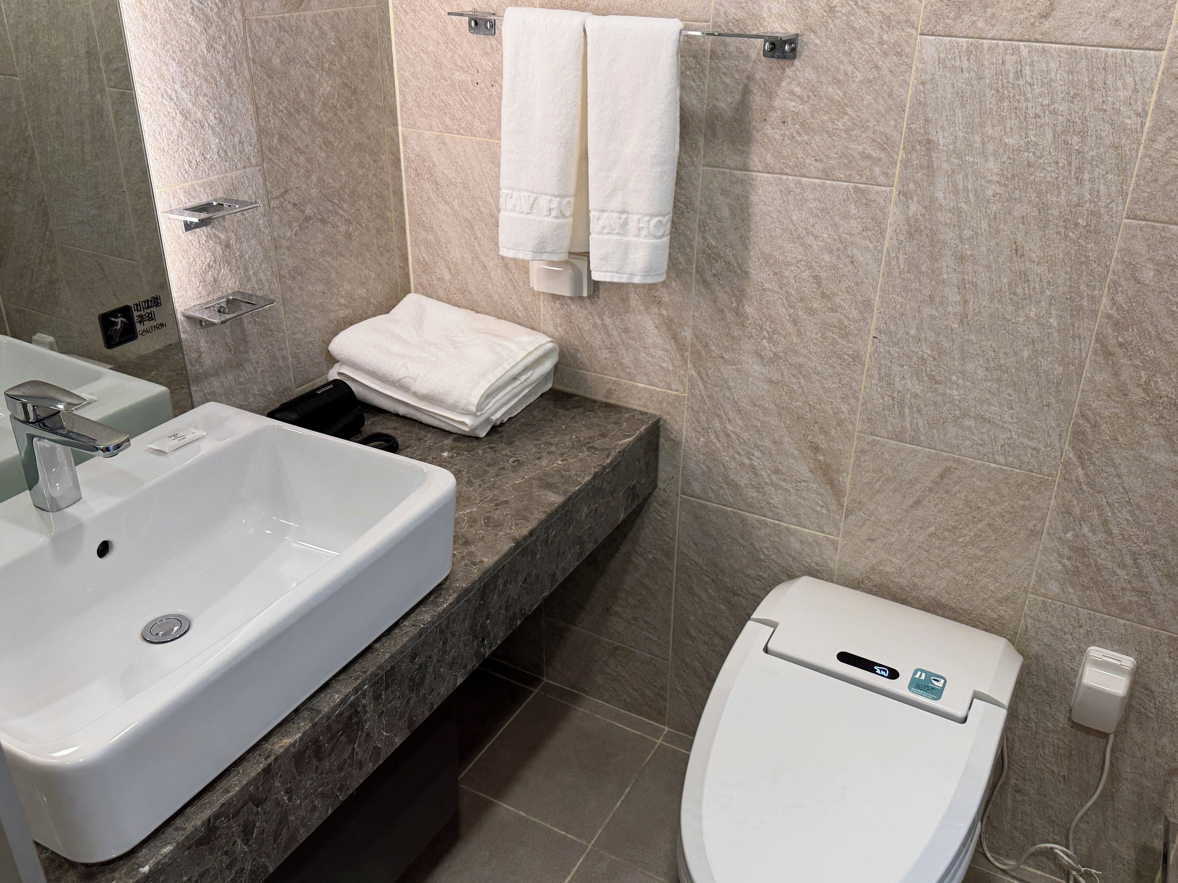 Ein Badezimmer mit einem weißen Waschbecken, einer Toilette und einem Handtuchhalter mit gefalteten Handtüchern.
