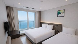 Een hotelkamer met een groot bed, een kleiner bed, een televisie en een raam met uitzicht op zee.