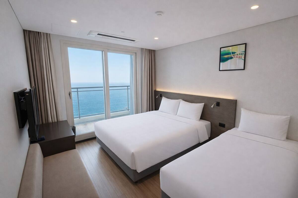 A hotel room with a large bed, a smaller bed, a TV, and a window with a view of the sea.