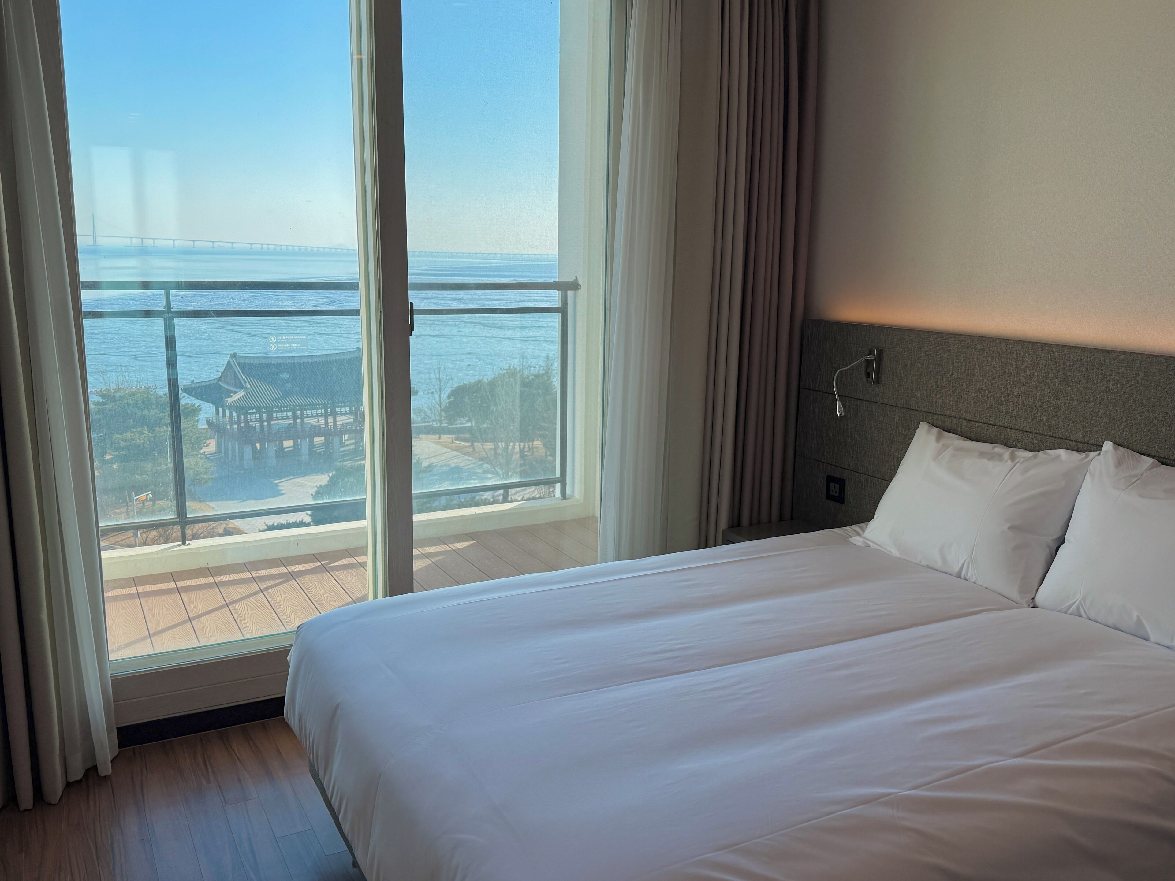 A hotel room with a large bed, a view of a body of water, and a traditional pavilion in the background.