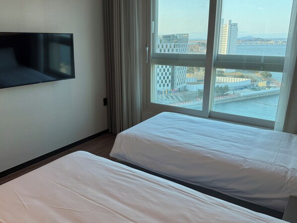 Une chambre d’hôtel avec deux lits, un téléviseur fixé au mur et une grande fenêtre donnant sur le paysage urbain et un pont.