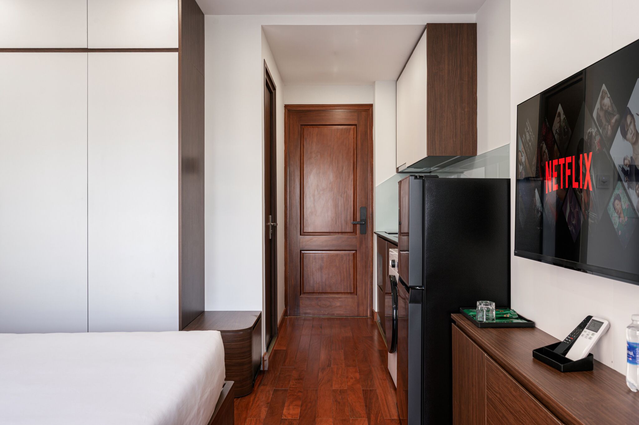 A hotel room with a bed, a minibar, a TV, and a door leading to another room.