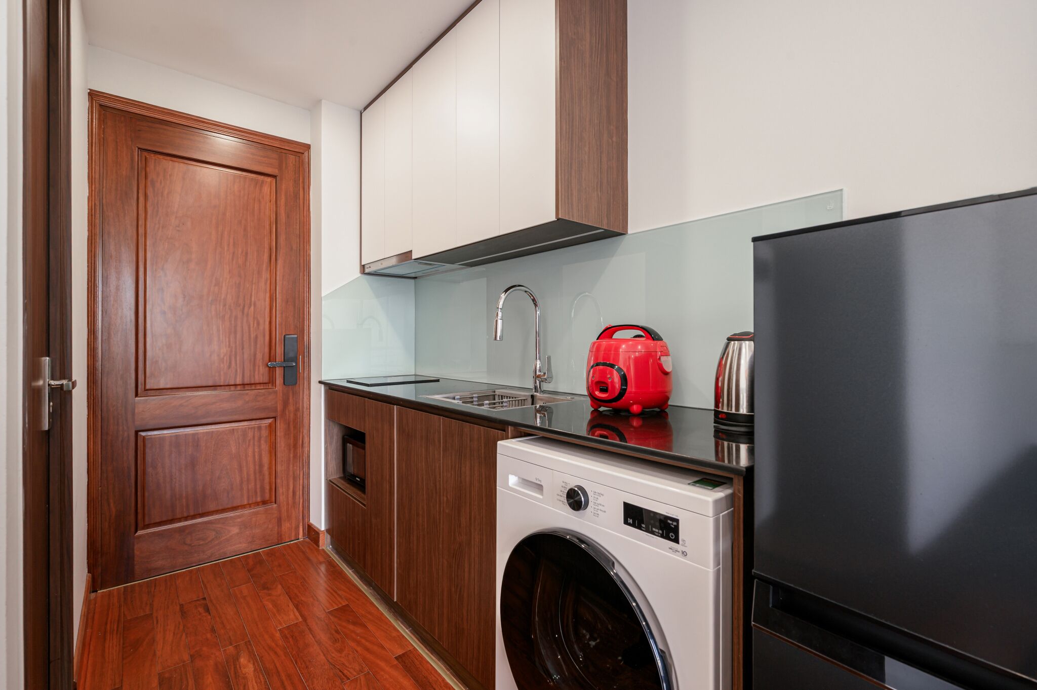 A compact kitchen with a washing machine, a red appliance, and a black refrigerator.