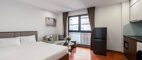 A hotel room with a bed, a sofa, a small table with a vase, a refrigerator, and a washing machine.