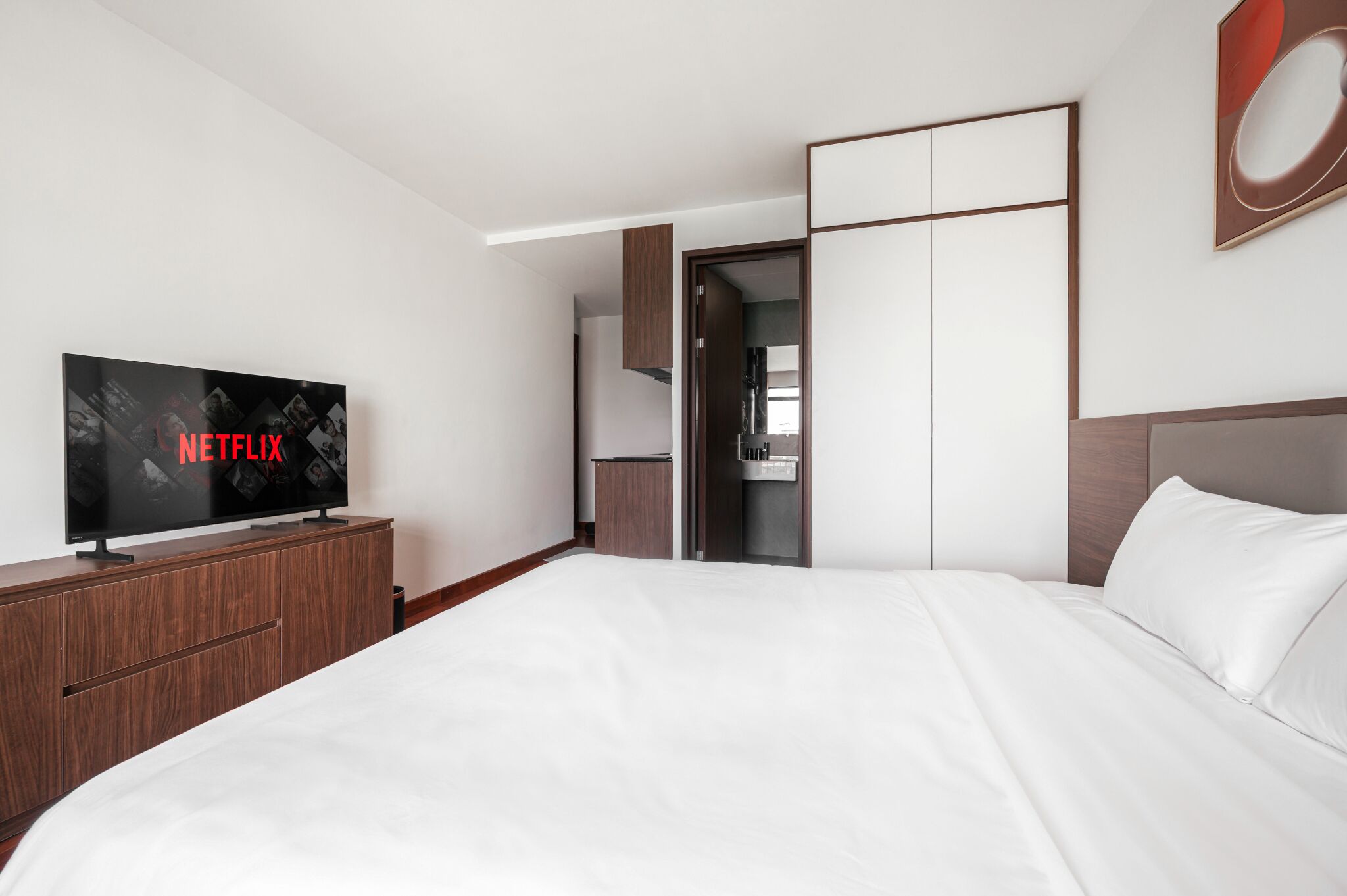 Moderni hotellihuone, jossa on suuri sänky, litteänäyttöinen televisio, josta voi katsoa Netflixiä, vaatekaappi ja kylpyhuone, joka näkyy avoimen oven läpi.