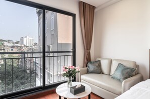A balcony with a city view, a sofa with cushions, a vase with flowers, and a tissue box on a small table. - Luxe Paradise Suites Doi Can (Ba Dinh)