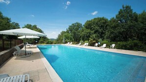 A rectangular swimming pool with clear blue water, surrounded by white lounge chairs and umbrellas, set against a backdrop of lush green trees and a clear sky. - Recent house surrounded by a natural park (Saint-Jean-de-Laur)