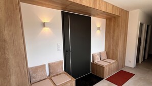 A modern hallway with wooden paneling, a black door, and seating areas with cushions. - Recent house surrounded by a natural park (Saint-Jean-de-Laur)