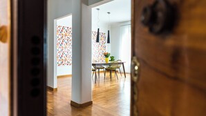 Et moderne spiseområde med et træbord og stole, en dekorativ væg med geometriske mønstre og hængende lamper.