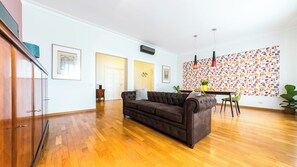 A spacious living room with a brown leather sofa, wooden flooring, a dining area with a table and chairs, and a colorful abstract wall art. - V3 - Flaminio Boutique | 10 Min Walk to Piazza del Popolo (Roma)