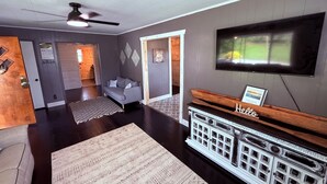 A living room with a fireplace, a television mounted on the wall, and a wooden bench with a sign that reads 'Hello'. - Wolf River Ridge on DHL 
1 minute from boat ramp! 
Kayaks & Bikes included (Byrdstown)
