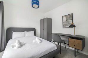 Una habitación de hotel con cama, escritorio, silla, armario y un cuadro en la pared.