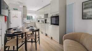 Cozinha moderna com armários brancos, área de jantar com mesa e cadeiras redondas, e uma janela grande.