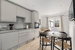 A modern kitchen with a dining area, featuring light-colored cabinetry, a built-in oven, and a round wooden table with two chairs. - Refurbished 4BDR Home in Harborne Birmingham (Birmingham)