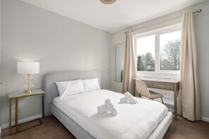 A hotel room with a bed, a desk, a chair, a lamp, and a window with curtains. - Refurbished 4BDR Home in Harborne Birmingham (Birmingham)