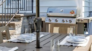 Un espace extérieur aménagé pour les repas, avec une table pour deux personnes, un barbecue et un escalier menant à une porte.