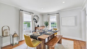 Un coin repas avec une table en bois dressée pour quatre personnes, entourée de chaises, d’un banc et d’une petite table d’appoint sur laquelle sont posées des bougies.