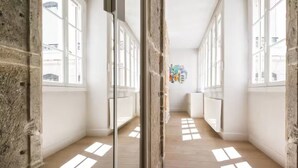 A narrow hallway with large windows, stone walls, and wooden flooring.