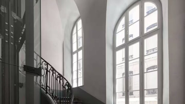 A staircase with ornate metal railings leading to a balcony with large arched windows.