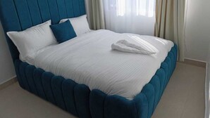 Un lit bien fait, avec une tête de lit rembourrée bleue et du linge de lit blanc.