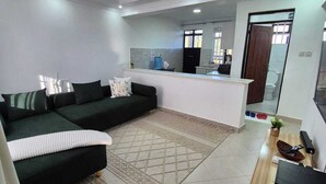 Un salon moderne avec un canapé d’angle vert foncé, un tapis blanc et un meuble TV en bois.