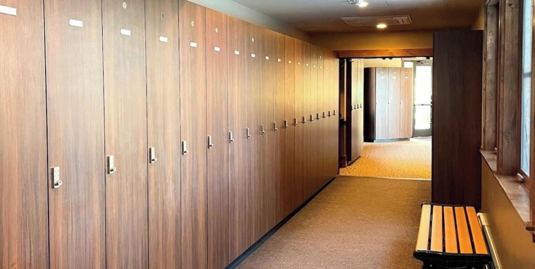 Un pasillo con taquillas de madera, un banco y piso alfombrado.