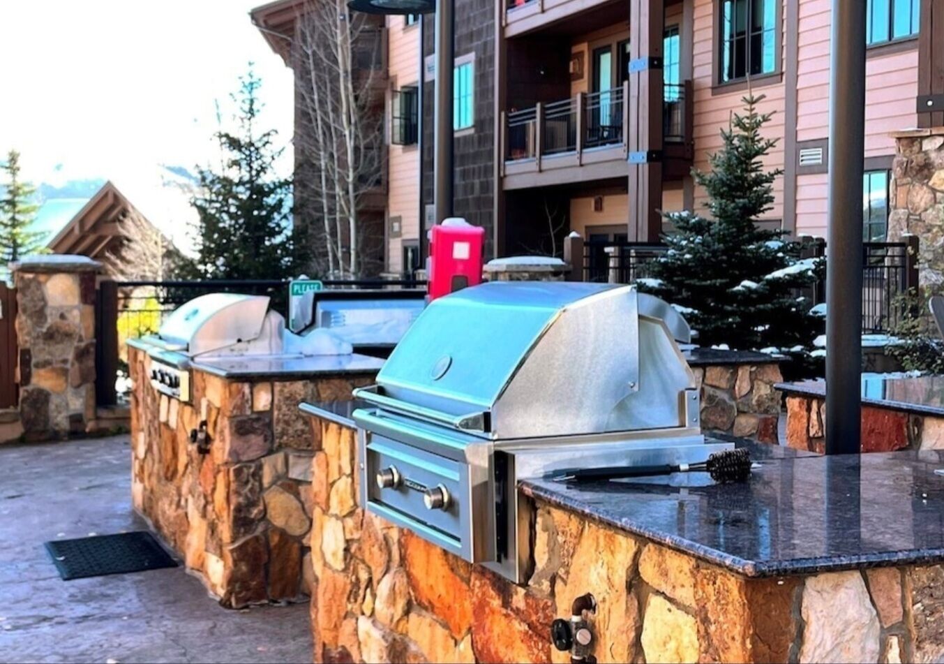 Un espace barbecue extérieur avec des murs en pierre et une vue sur un immeuble à plusieurs étages en arrière-plan.