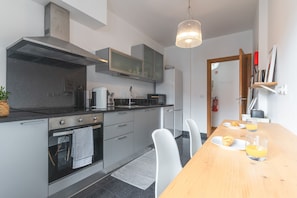 A modern kitchen with a built-in oven, microwave, and stainless steel range hood. There is a dining table with chairs and two glasses of orange juice. - Garajau Comfort Stay by Atlantic Holiday (Caniço)