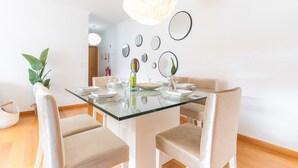 Et moderne spiseområde med et glasbord, beige polstrede stole og flere vægmonterede spejle.