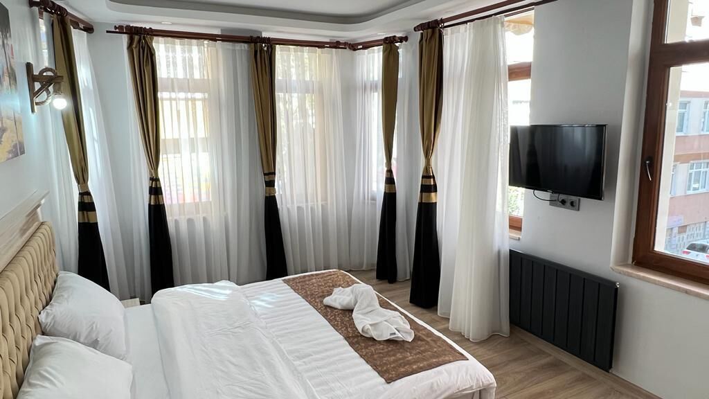 Quarto de hotel com cama grande, cortinas, televisão e janela.