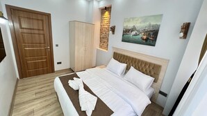 A neatly made bed with white linens, a wooden wardrobe, a painting of a harbor scene, and a stone accent wall. - Mar Suite (İstanbul)