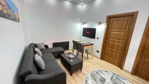 En moderne stue med en hjørnesofa, et lille bord, et fjernsyn og en dør.