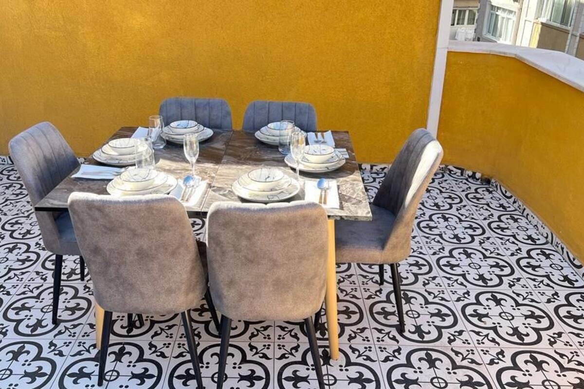 A dining table set for six with chairs, a yellow wall, and patterned floor tiles.
