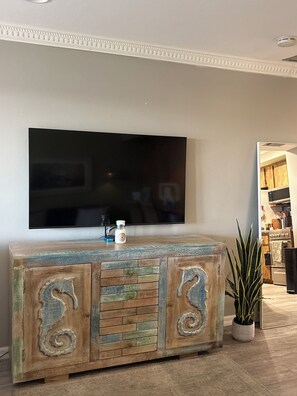 Ein Wohnzimmer mit einem an der Wand befestigten Flachbildfernseher, einem Holzschrank mit dekorativen Schnitzereien und einem Blumentopf.