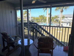 Ein Balkon mit Korbmöbeln, einem Glastisch und Blick auf einen Pool und Palmen.
