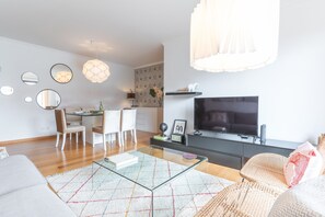 Un salon moderne avec une table basse en verre, un téléviseur à écran plat, un coin repas avec des chaises et un comptoir de cuisine.