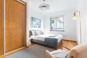 Une chambre à coucher comprenant un lit, une table de chevet, une chaise, une fenêtre et un luminaire suspendu.