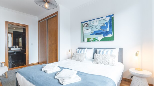 Ein modernes Hotelzimmer mit einem großen Bett, einem Badezimmer mit Spiegel und Waschbecken sowie einem Bild an der Wand.