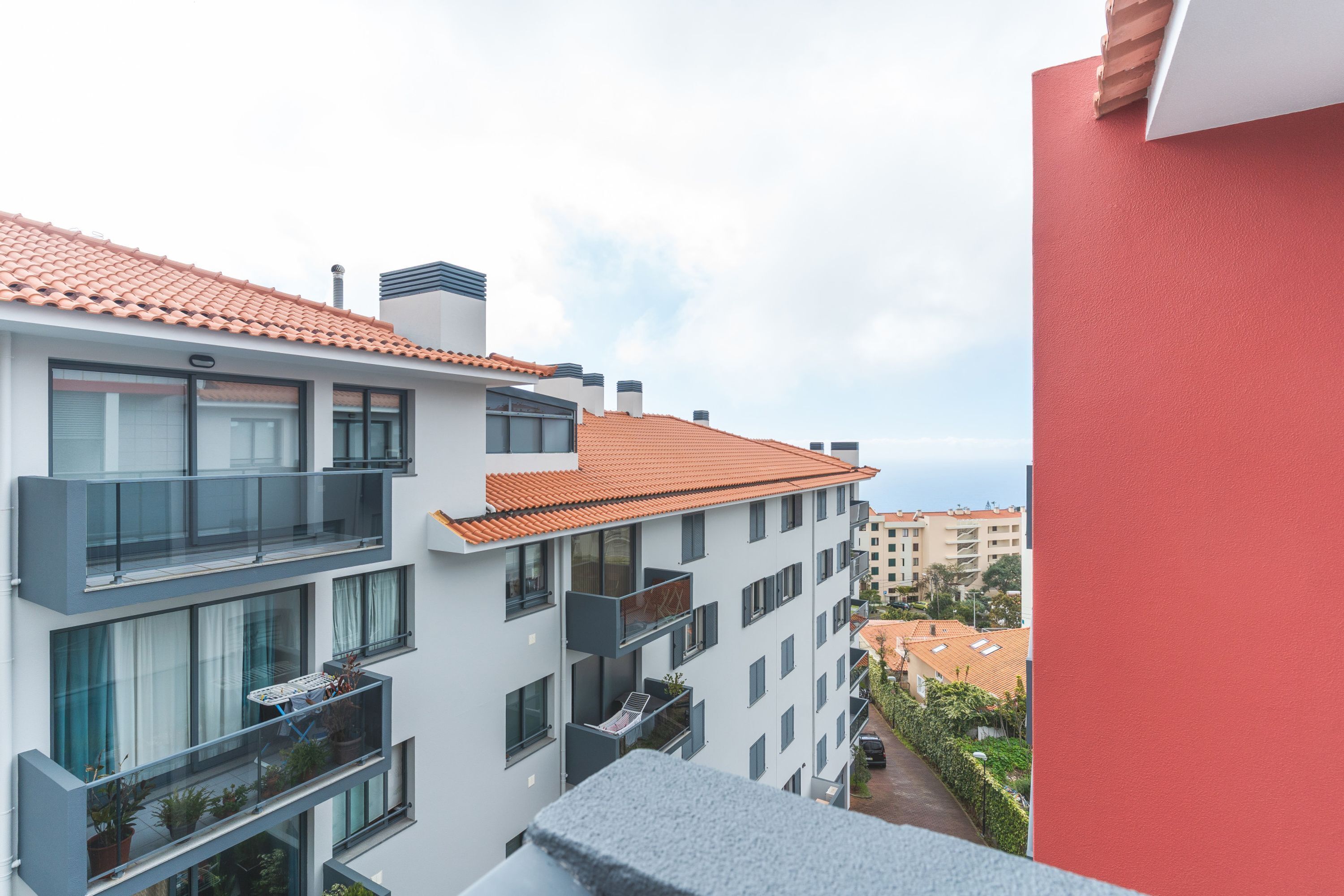 A multi-story building with balconies, large windows, and a red-tiled roof.