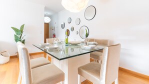 Ein moderner Essbereich mit einem Glastisch, beige gepolsterten Stühlen und verschiedenen wandmontierten Spiegeln.