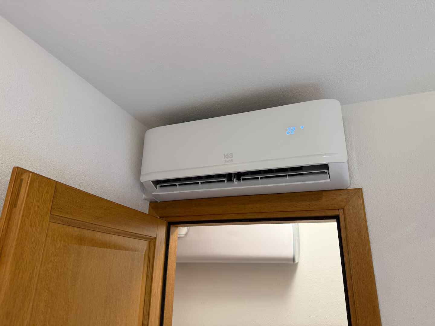 Een witte airconditioningunit bevestigd aan een muur boven een houten deur.
