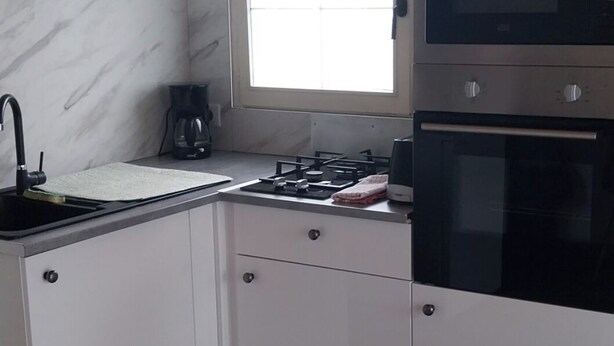 Una cocina compacta con gabinetes blancos, estufa a gas, microondas y una ventana.