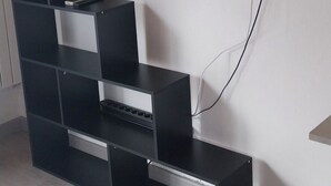 Una sala de estar moderna con un televisor de pantalla plana montado en la pared, un mueble de entretenimiento negro con estantes, y piso de madera.