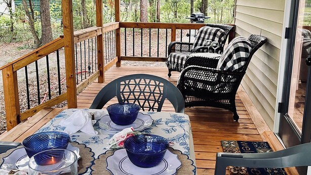 A covered outdoor deck with a table set for dining, surrounded by chairs, and a grill in the background. - New Cottage within minutes from our Famous Springs! (Fort White)