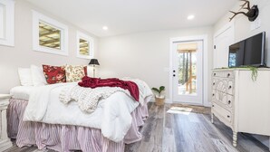 A bedroom with a bed, dresser, TV, and a door leading outside. - New Cottage within minutes from our Famous Springs! (Fort White)