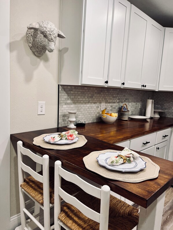 A kitchen with white cabinets, a marble backsplash, and a wooden dining table with two chairs.
