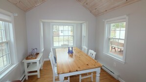 Ein Esszimmer mit Holztisch, weißen Stühlen, großen Fenstern und einer weißen Decke.
