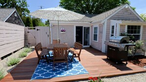 Ein Garten mit einer Holzdielenveranda, einem überdachten Patio, einem Grill und einem kleinen Schuppen.