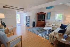 A spacious living room with a wooden floor, a sofa set, a coffee table, and a television.