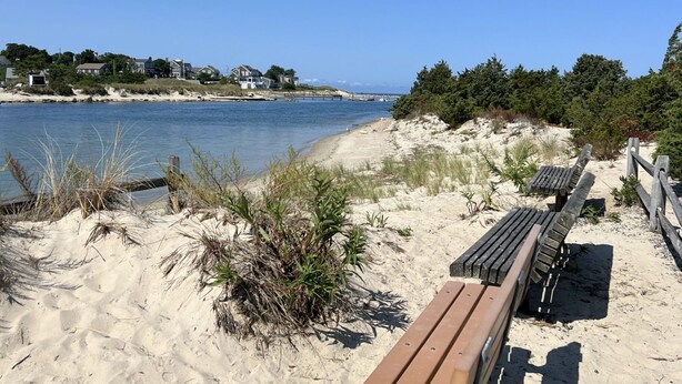 Ein sandiger Strand mit hölzernen Bänken und einer Holzpromenade, die zum Wasser führt.